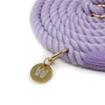 Load image into Gallery viewer, Close-up of a purple braided rope leash with a gold tag featuring The Woofdrobe logo on a white background